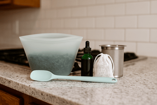 Home cannabis infusion tools on a kitchen counter, including a silicone pouch with herbs, dark green dropper bottle, mesh strainer, cloth sachet, and spatula.